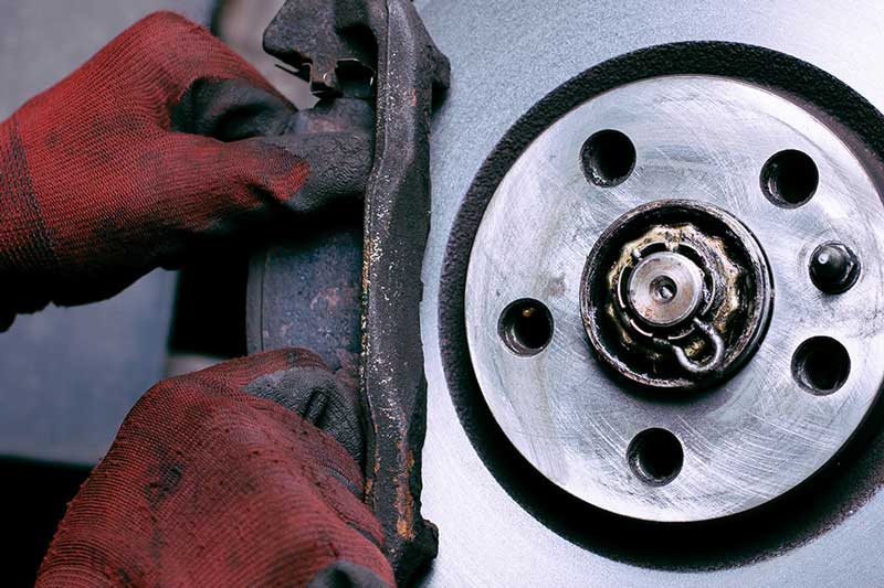 Gloved hands working on a car's brake caliper next to a shiny brake rotor and wheel hub.